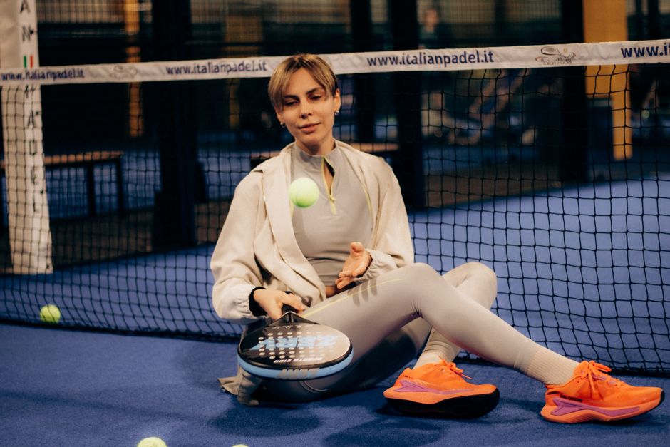 Een sportieve vrouw in langere padelbroeken speelt padel op een zonnige dag, met een padelracket in de hand.